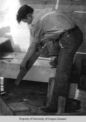 Students building a house, Berea College: man sawing