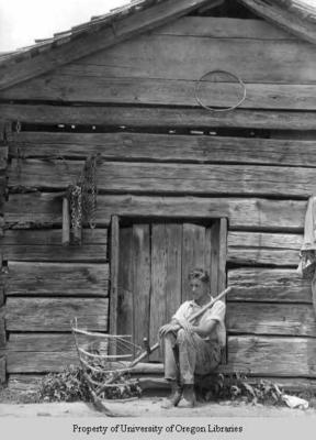 Hatcher: young man with hay rake sitting outside shed